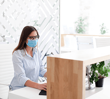 Receptionist wearing medical mask in office.